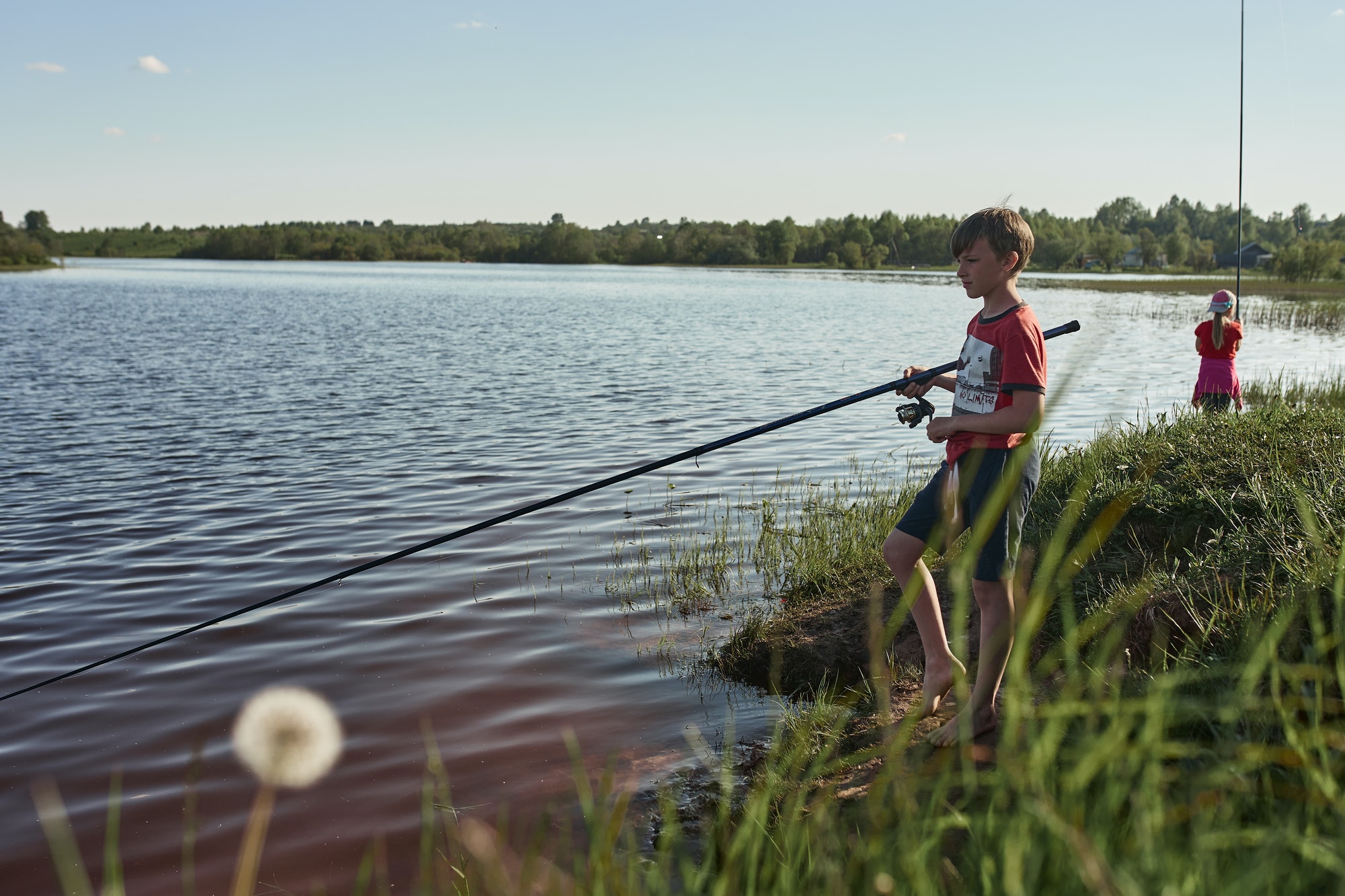 Children fishing on the shore of a large lake.